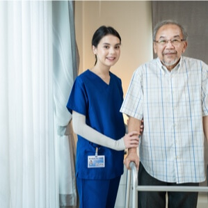 Skilled Nurse Helping Elderly Man Walk in Assisted Living Facility Skilled Nurse Helping Elderly Man Walk in Assisted Living Facility